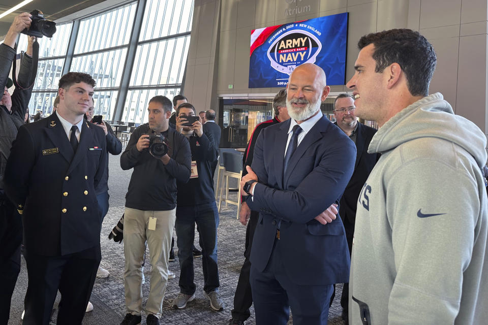 New England Patriots long snapper Joe Cardona, right, a Navy graduate and active member of the Naval Reserves, greets Navy coach Brian Newberry, second from right, during a news conference at Gillette Stadium in Foxborough, Mass., Wednesday, Nov. 29, 2023, for the Army-Navy NCAA college football game, which will be held in Foxborough on Dec. 9. At left looking on is Navy linebacker Will Harbour. (AP Photo/Jimmy Golen)