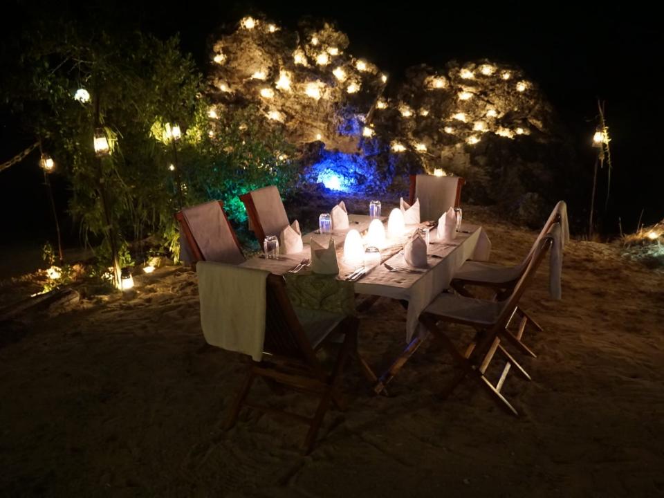 A table set up for dinner on the sand lit by candles with a romantic ambiance.