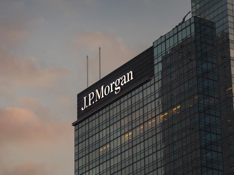 A glass office building at dusk, with JPMorgan logo in white on a black background on its top corner.