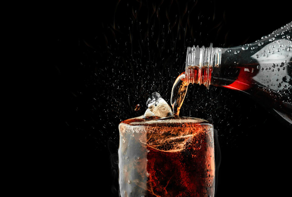 A bottle of cola being poured into a glass.