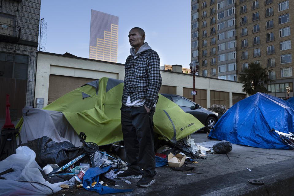 FILE - Carlos, a homeless man stands in front of his tent in Portland, Ore., on June 4, 2021. Growing discontent over homelessness, crime and protests in Portland is driving interest in a pair of congressional primaries in the state. (AP Photo/Paula Bronstein, File)