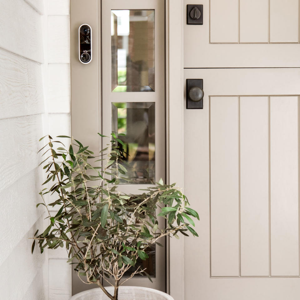 Arlo wireless video doorbell mounter beside a front door with a potted olive tree underneath