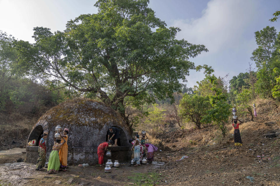 Women gather near a well to draw water as others walk home carrying pots of water on their heads in the village of Bibalvadi, northeast of Mumbai, India, Saturday, May 6, 2023. The village is more than an hour's hike away for these women who walk as quickly and steadily as they can back to their homes, made of red brick, which offer a bit of respite from the extreme heat. (AP Photo/Dar Yasin)