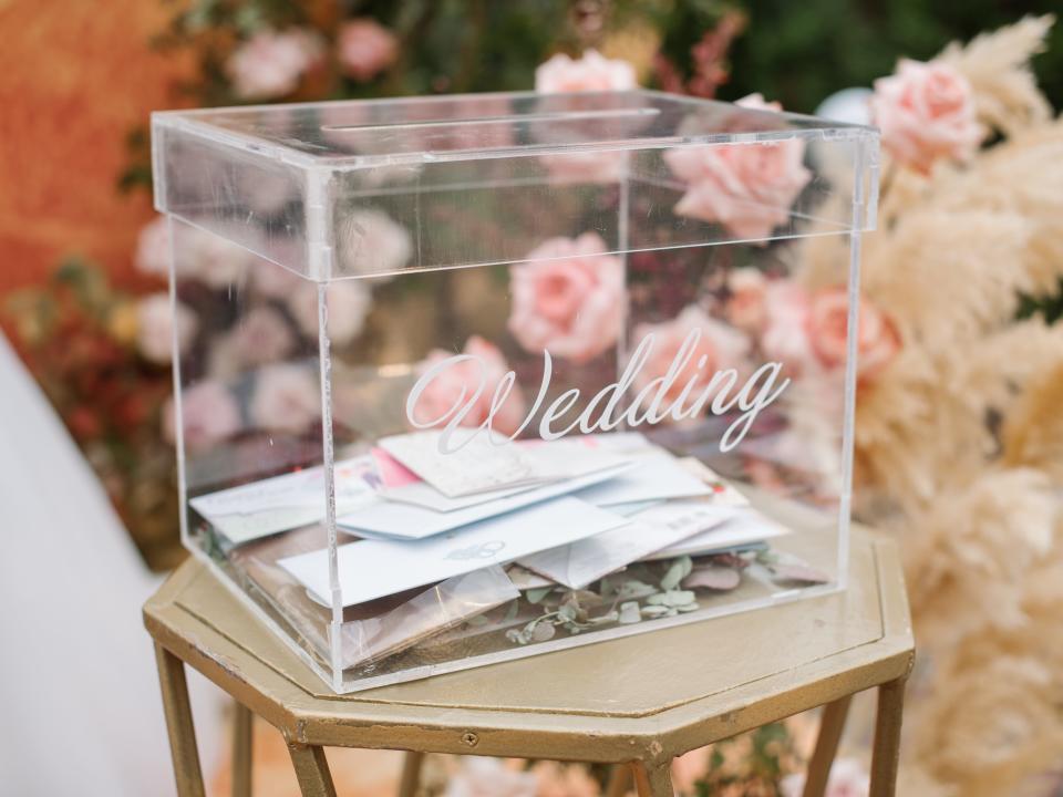 An acrylic card box marked "Wedding," with cards inside, sits on a small table.