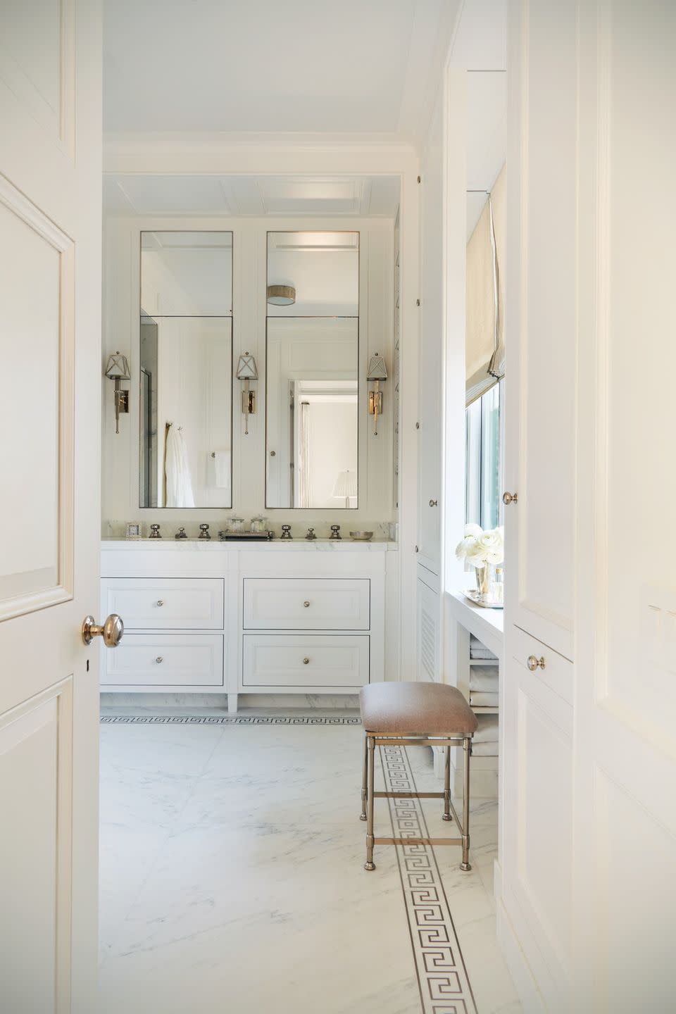a large bathroom is decorated with marble floors with greek key detail on the border and tall mirrors