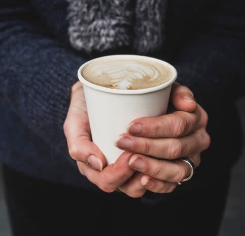 Person holding a paper cup with steamed milk leaf design on coffee