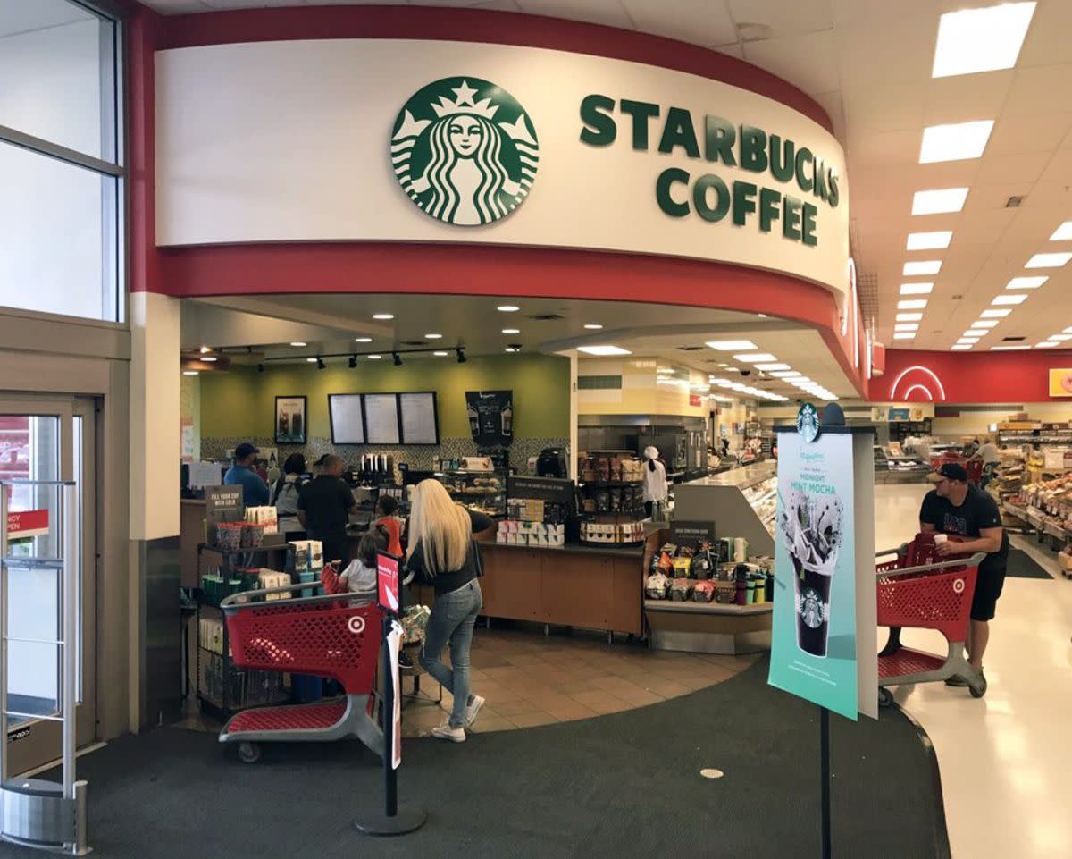 A Starbucks cafe in a Target store, entrance doors to the left, produce section in the background to the right, people with shopping carts waiting around