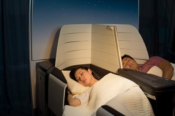 A man and a woman resting in lie-flat airplane seats
