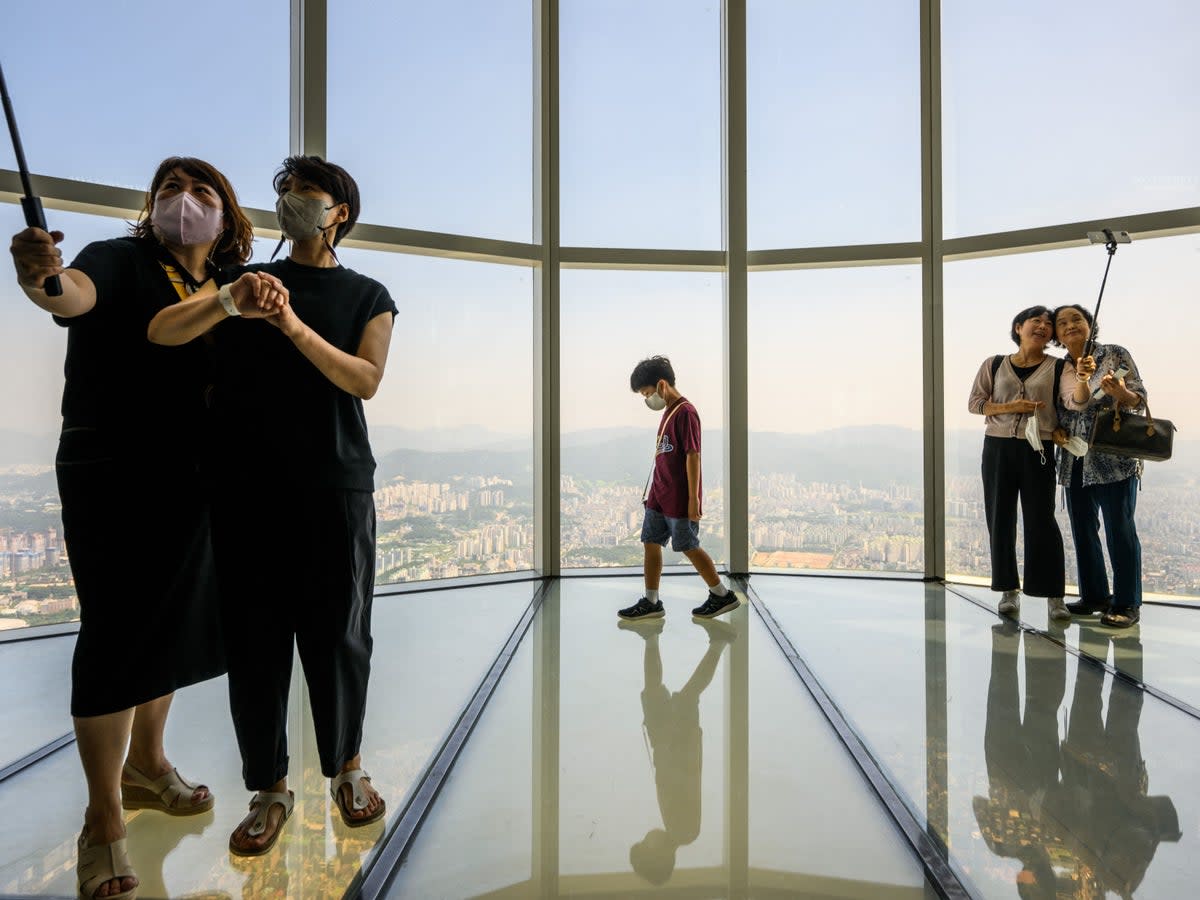 File. People pose for selfies at the Lotte World Tower Seoul Sky on 12 August 2022. - South Korean government has decided to pay an allowance to reclusive youths to help them get out of their homes (AFP via Getty Images)