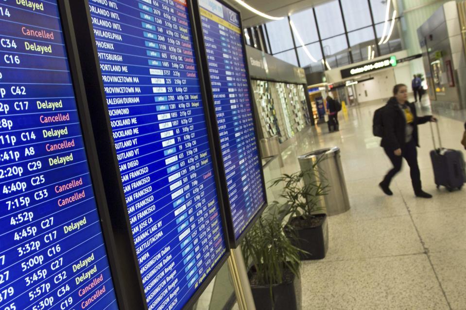 A woman walks past a flight information board displaying delays and cancellations at Logan International Airport during a winter nor'easter snow storm in Boston