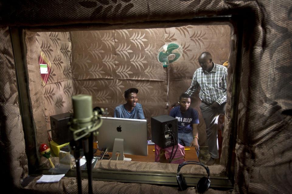 In this photo taken Monday, March 24, 2014, students Innocent Nzayisenga, 21, left, and Theoneste Ni Yomushumba, 18, right, talk to school Director Jean Claude Nkulikiyimfura, standing, as they practice in the music recording studio at the Agahozo-Shalom Youth Village near Rwamagana, in Rwanda. Most of the kids in a Rwandan school set amid the lush green, rolling hills of eastern Rwanda don’t identify themselves as Hutu or Tutsi. That’s a positive sign for Rwanda, which is now observing the 20th anniversary of its genocide, a three-month killing spree that, according to the official Rwandan count, left more than 1 million people dead, most of them Tutsis killed by Hutus. The teenagers attending the Agahozo-Shalom Youth Village, a school with dorms that creates tight-knit student families, say the ethnic slaughter that their parents or grandparents were a part of either as victims or perpetrators won’t be repeated. The school director echoes the sentiment. (AP Photo/Ben Curtis)