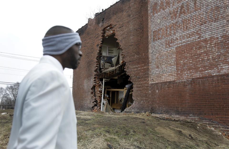 In this Thursday, Jan. 16, 2014 photo, Melvin White, founder of the Beloved Streets of America project, walks past crumbling building during a tour of Dr. Martin Luther King Jr. Drive in St. Louis. The nonprofit is working to revitalize a downtrodden six-mile stretch of the drive named for the slain civil rights leader, marked by vacant lots, crumbling buildings and a preponderance of liquor stores, pawn shops and check-cashing businesses. Project leaders hope revitalize MLK's streets that have fallen into disrepair in cities around the country. (AP Photo/Jeff Roberson)