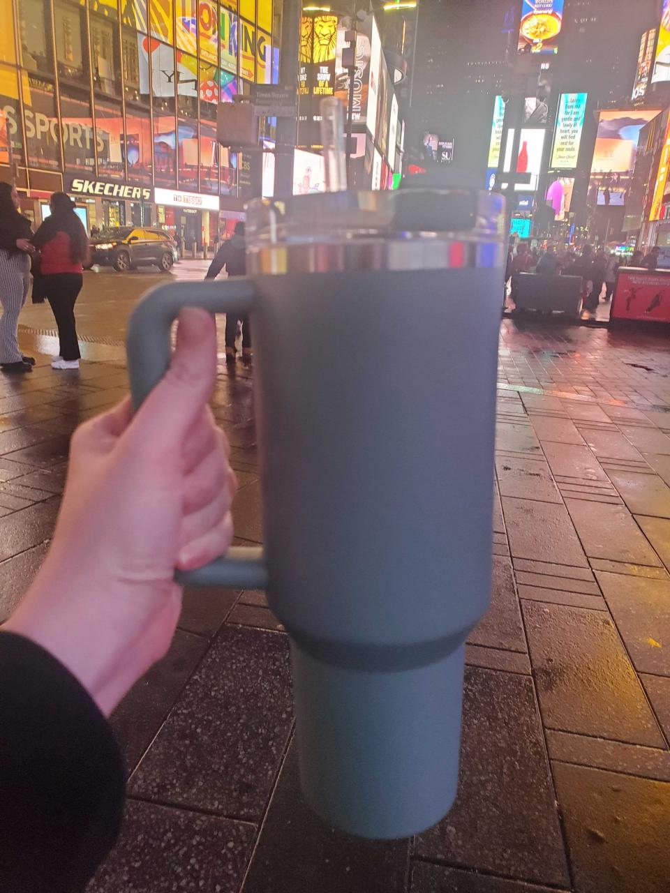 A woman's hand holding a teal Stanley cup while she walks in New York City.