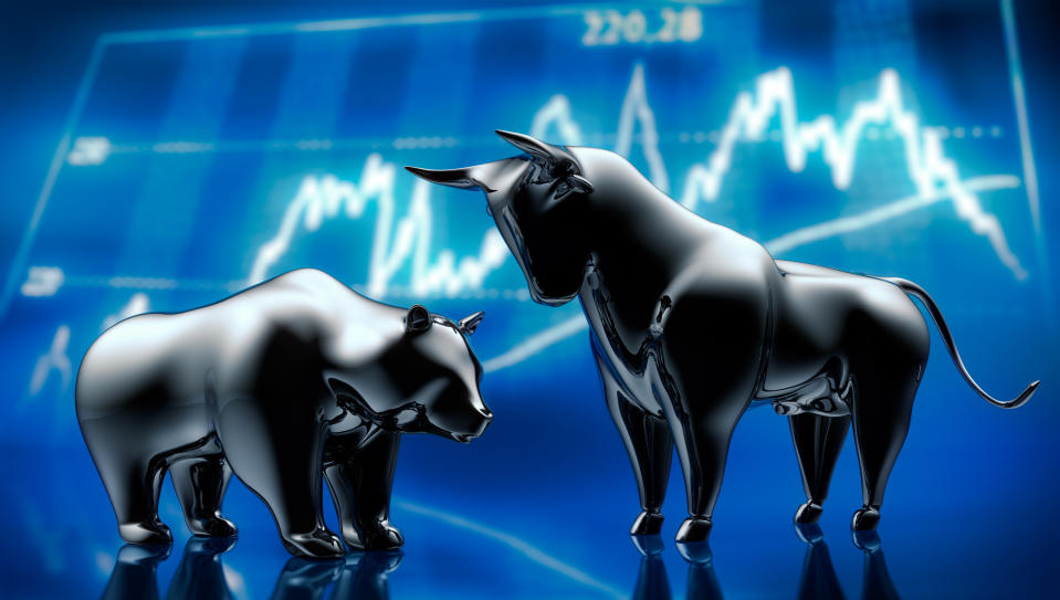 Silver bull and bear sculptures standing in front of a dark blue stylised stock market graphic.