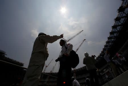 Workers and media memebers are seen under the light of the sun during a heat wave, at the construction site of the New National Stadium, the main stadium of Tokyo 2020 Olympics and Paralympics, during a media opportunity in Tokyo, Japan July 18, 2018. REUTERS/Issei Kato