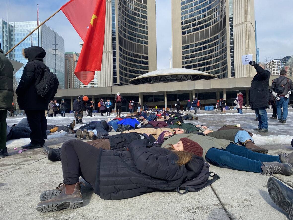 Advocates for the unhoused are seen here taking part in a 'die-in' at Toronto city hall on Monday. They are urging city council to expand the hours of its warming centres until April. (Shawn Jeffords/CBC - image credit)