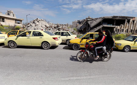 Men ride a motorbike past cars, in line at a gasoline station, waiting to fuel up in Aleppo, Syria April 11, 2019. Picture taken April 11, 2019. REUTERS/Omar Sanadiki