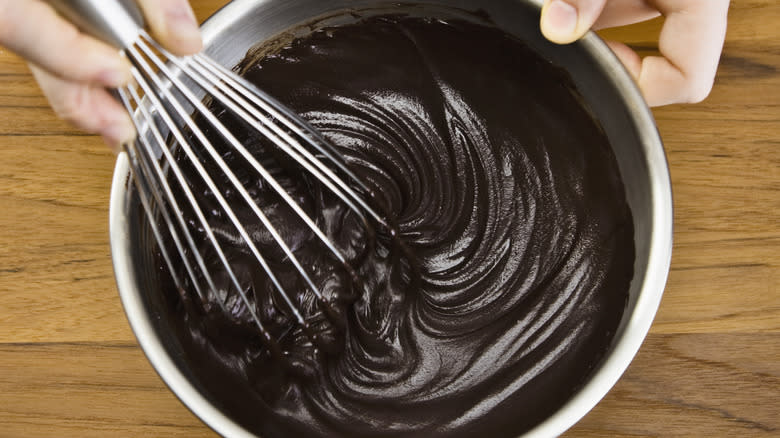 A hand whisking a bowl of chocolate ganache