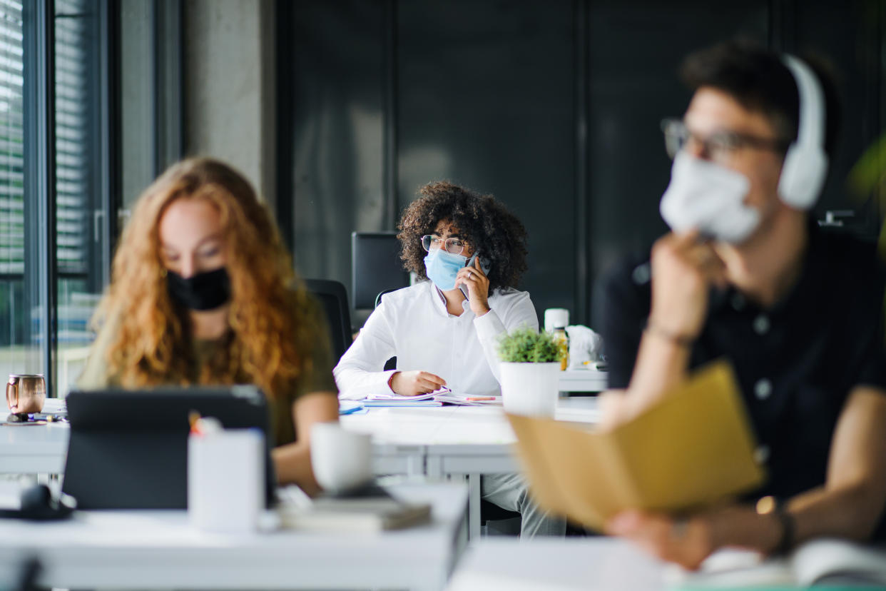 Young people with face masks back at work in office after coronavirus quarantine and lockdown.