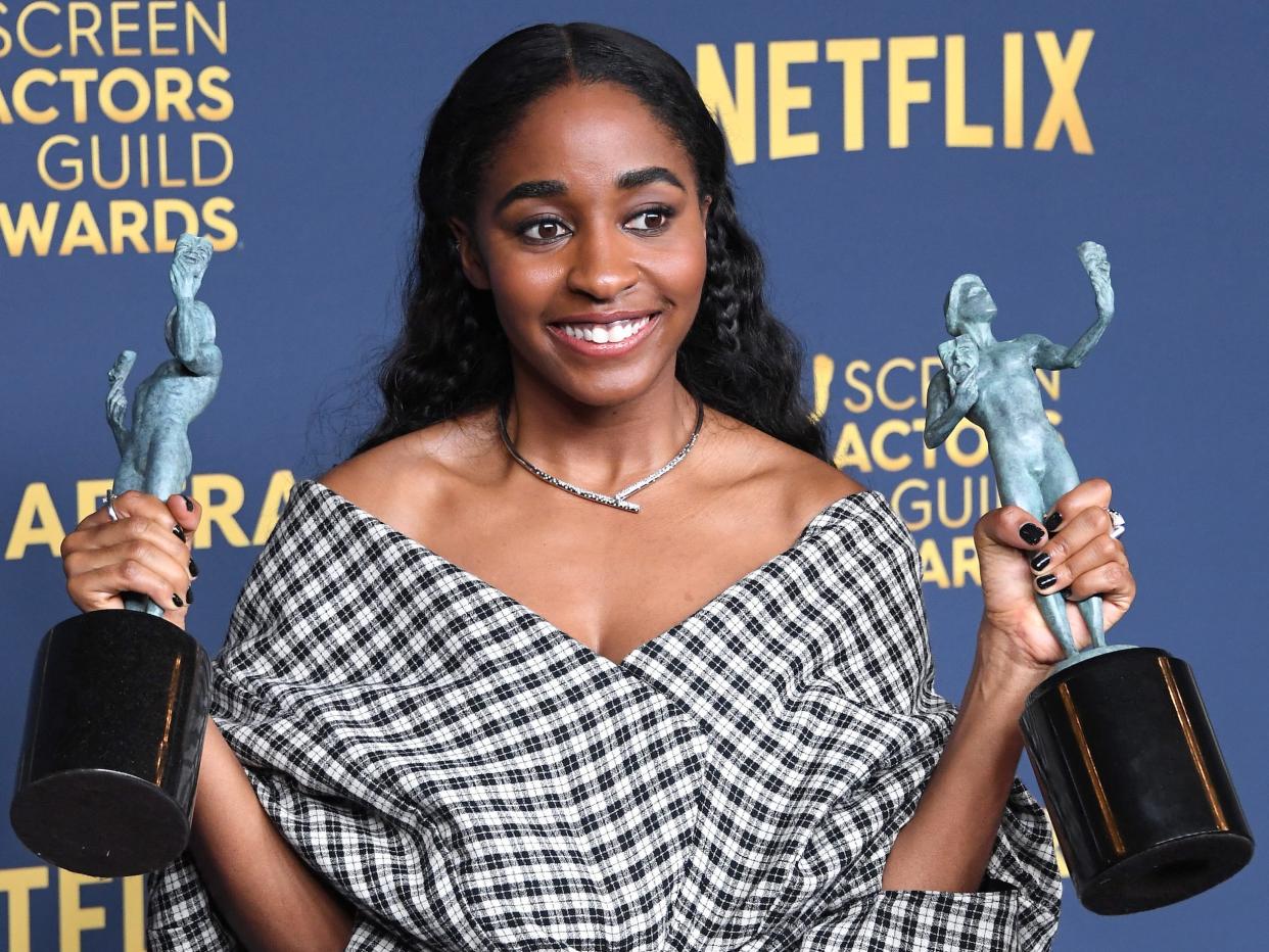 Ayo Edebiri in a black and white off-the-shoulder checkered dress holding up two green trophies