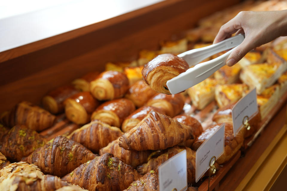 Cropped image of an Asian young woman buying pastry from a cafe selecting holding a tray and service tong