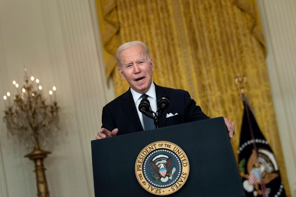 President Biden speaks into a microphone in the East Room of the White House.