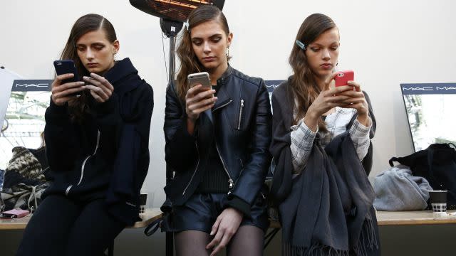 Models look at their mobile phones backstage before the Guy Laroche Spring/Summer 2016 women's ready-to-wear...