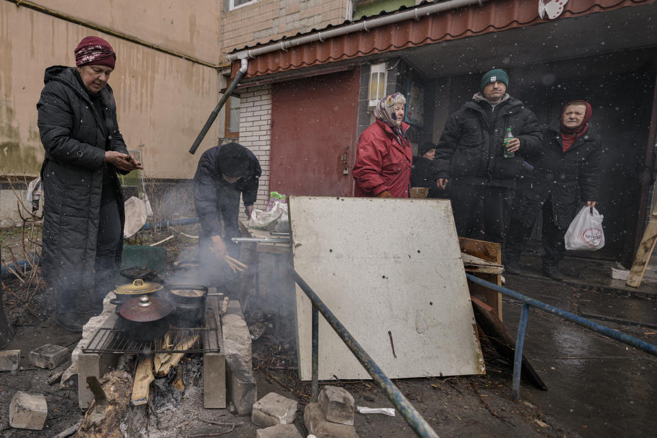 People cook on an open fire outside an apartment building which had no electricity, water or gas since the beginning of the Russian invasion in Bucha, Ukraine, Sunday, April 3, 2022. (AP Photo/Vadim Ghirda)