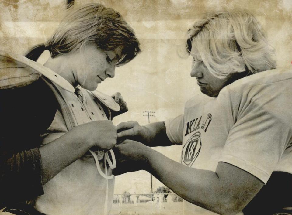 In a 1976 file photo, Oklahoma City dolls football player Cindee Herron helps teammate Terri Talley fasten her shoulder pads.