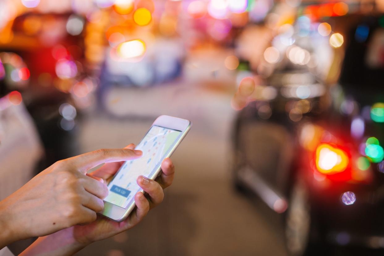 Hands holding a phone using the Uber app. The background shows car and city lights.