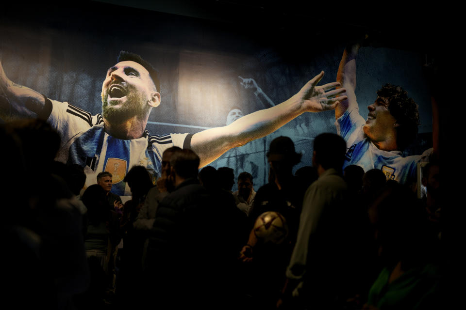 Journalists walk past photos of soccer player Lionel Messi, left, and late soccer star Diego Maradona as they enter the exhibit titled "Campeones del Mundo," or World Champions at Exposition Center in Buenos Aires, Argentina, Wednesday, April 5, 2023. World Champions is the first official exhibition by the Argentine Soccer Association (AFA) that displays the history of the three world cups won by the national team. (AP Photo/Natacha Pisarenko)