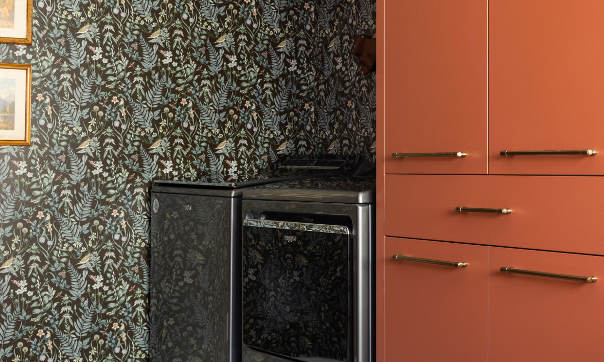  A laundry room with orange cabinetry and wallpaper. 