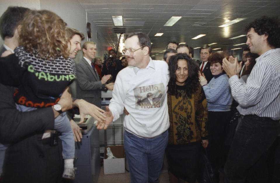 FILE - Wearing a "Hello World" sweatshirt printed with his picture, former hostage Terry Anderson greets colleagues, Dec. 10, 1991, at The Associated Press headquarters in New York, as he walks with his arm around fiancée Madeleine Bassil, center right. Fellow former hostages, family, and coworkers celebrated the life of journalist and philanthropist Terry Anderson, Wednesday, May 8, 2024, as a man who helped others while struggling to heal himself. (AP Photo/Ron Frehm, File)