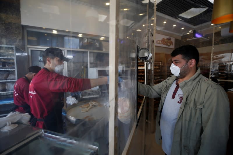 A Palestinian customer, wearing a mask as a preventive measure against the coronavirus disease, buys bread in a bakery in Gaza City