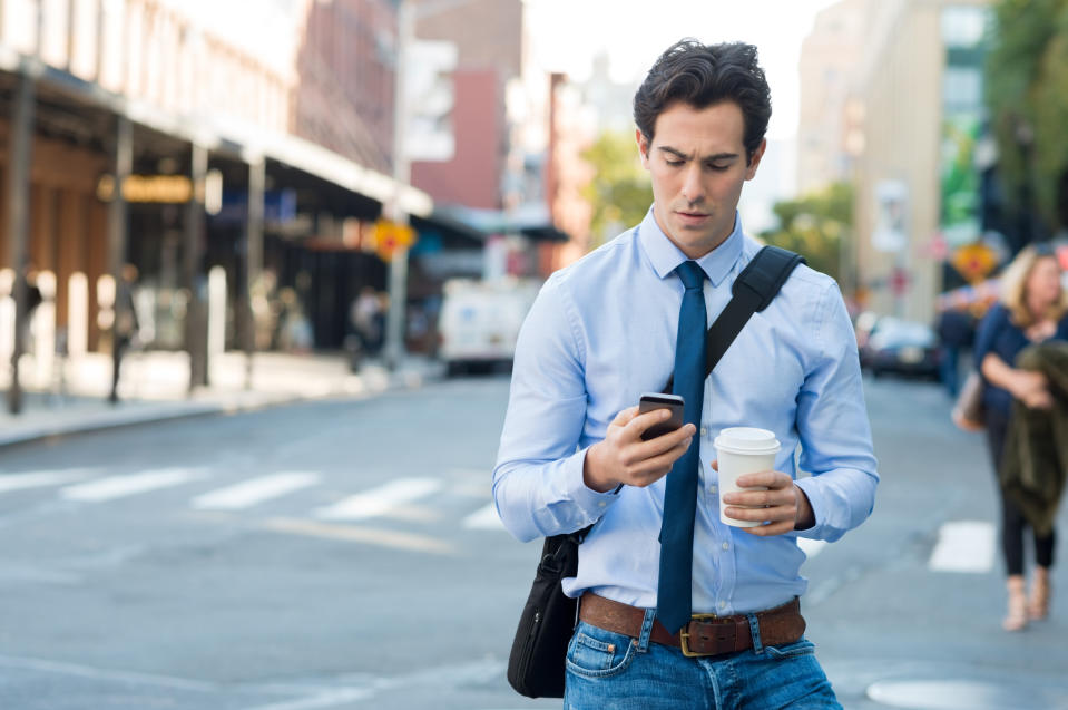 A young man looking at his smartphone on the street.