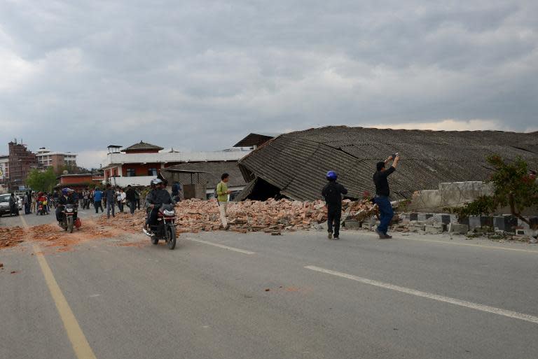 Nepalese people walk past a collapsed building in Kathmandu, on April 25, 2015