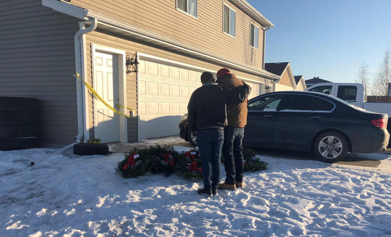 Two friends of seven people whose bodies were found in a Moorhead, Minn., home comfort each other next to seven wreaths that were left outside the residence on Monday, Dec. 20, 2021. Police say four adults and three children died but they have not released the cause of their deaths. Relatives say they still have more questions than answers about what happened. (AP Photo/Dave Kolpack)