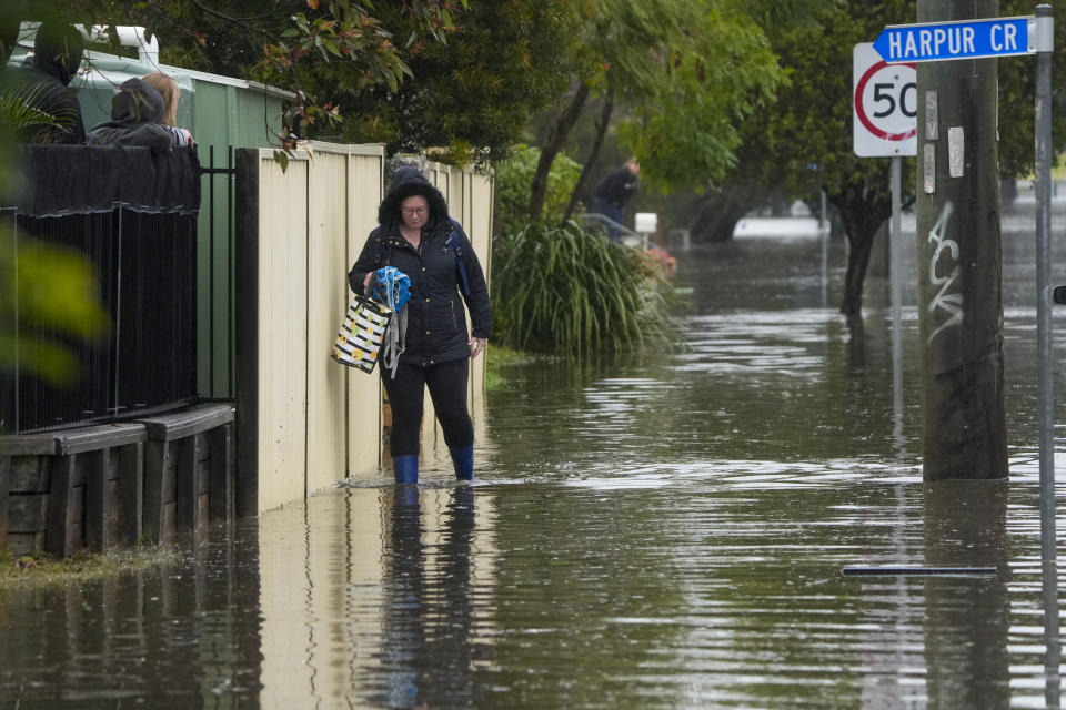 A woman walks through flood waters outside her house at Windsor on the outskirts of Sydney, Australia, Tuesday, July 5, 2022. Hundreds of homes have been inundated in and around Australia's largest city in a flood emergency that was threatening 45,000 people, officials said on Tuesday. (AP Photo/Mark Baker)