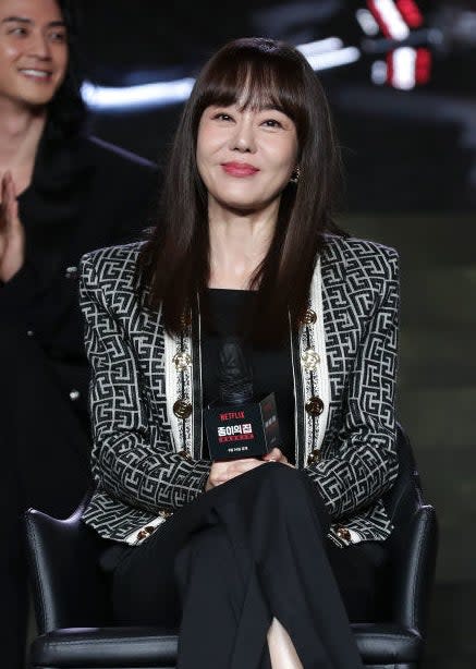 Yunjin with long hair, bangs, and wearing a fancy designer suit sitting on a panel at a Netflix Korea event