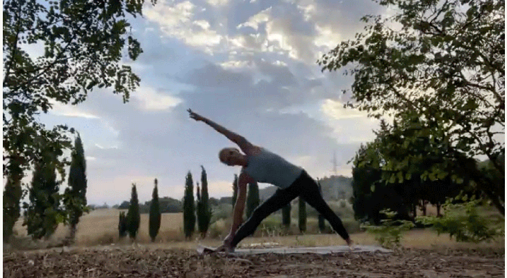 Woman practicing yoga outside at sunrise with her top arm extended alongside her ear