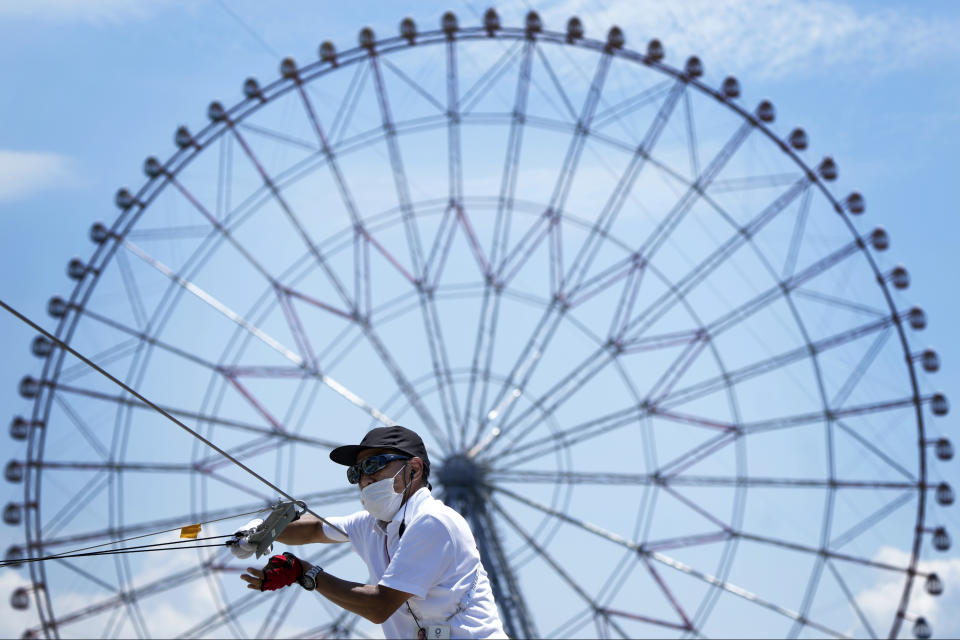 An official wears a mask and gloves as he prepares the cables for the gates on the competition course at the Kasai Canoe Slalom Centre at the 2020 Summer Olympics, Saturday, July 24, 2021, in Tokyo, Japan. (AP Photo/Kirsty Wigglesworth)