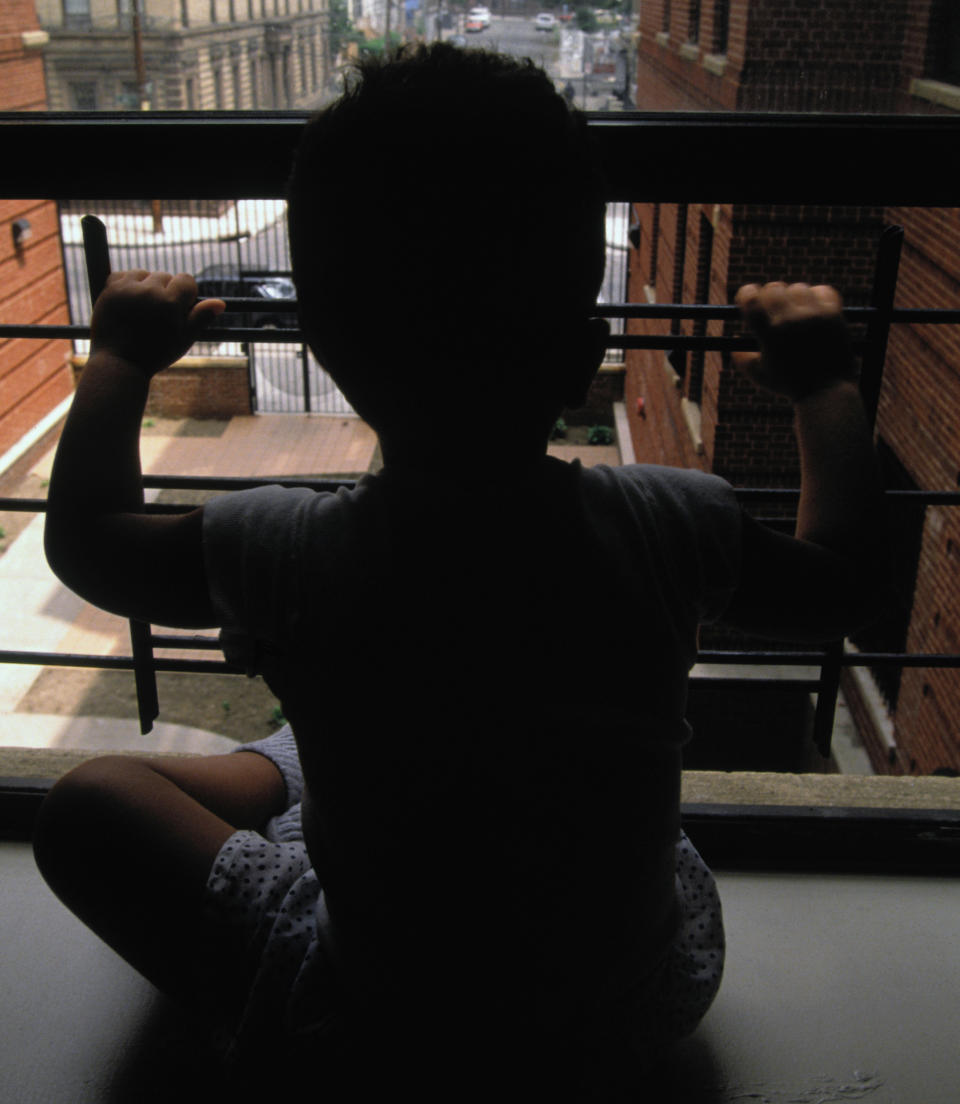 A toddler looks out from a balcony.