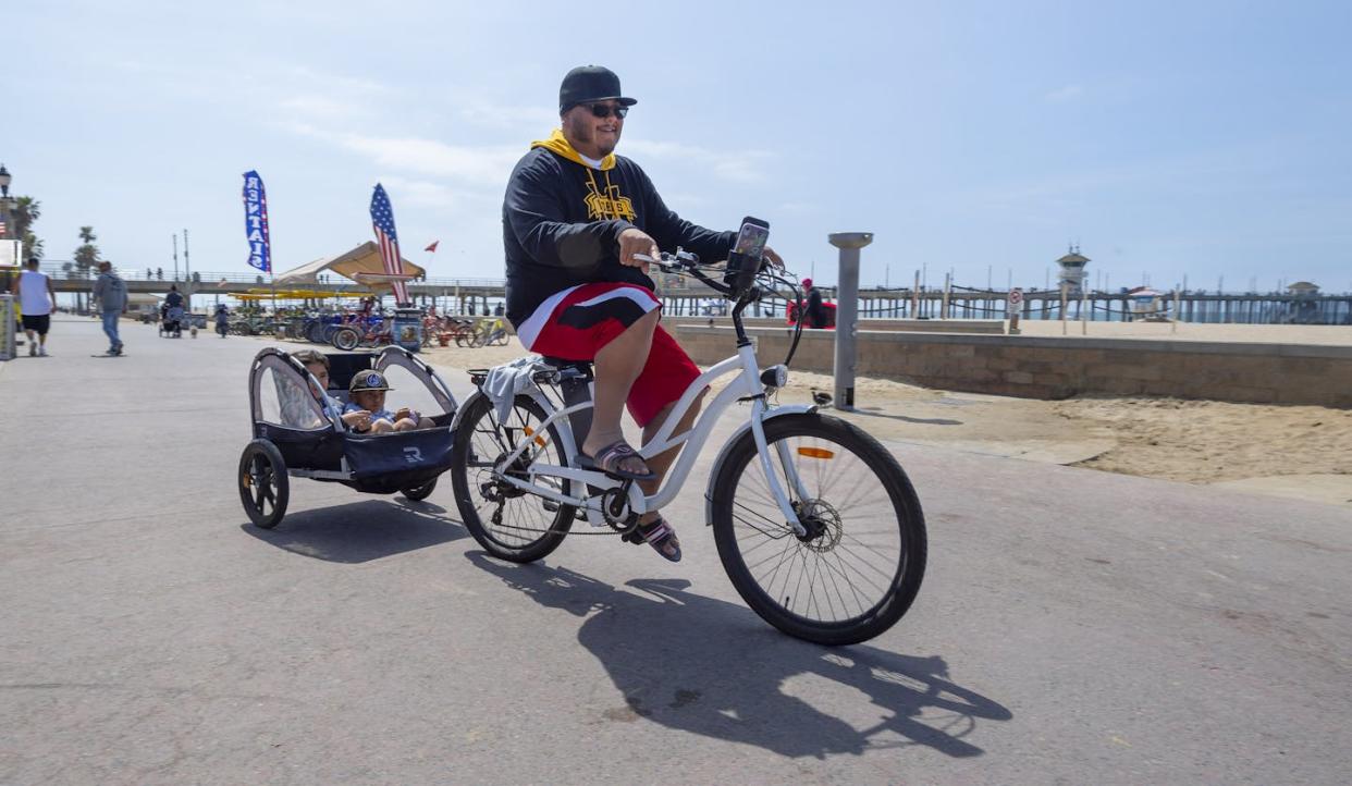 A man pulls his kids behind an electric bicycle near the pier in Huntington Beach, Calif. <a href="https://www.gettyimages.com/detail/news-photo/man-pulls-his-kids-behind-an-electric-bicycle-near-the-pier-news-photo/1311180585" rel="nofollow noopener" target="_blank" data-ylk="slk:Paul Bersebach/Orange County Register via Getty Images;elm:context_link;itc:0;sec:content-canvas" class="link ">Paul Bersebach/Orange County Register via Getty Images</a>