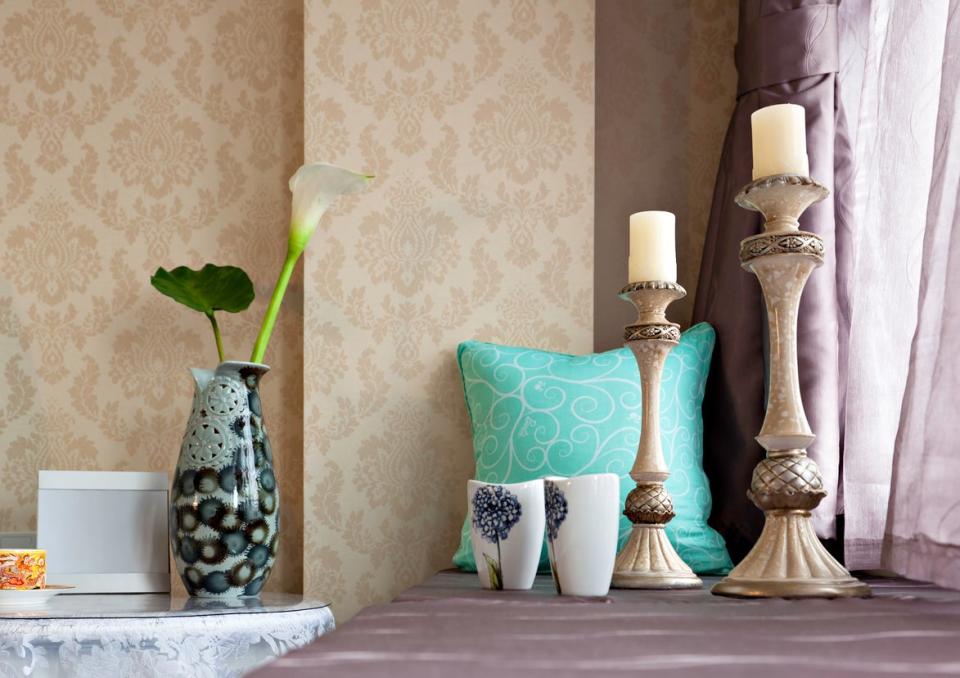 Two candles on a windowsill with purple curtains and beige wallpaper.
