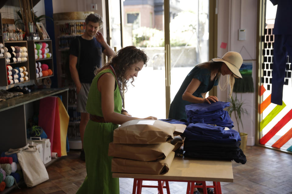 Textile artist Brooke Dennis, centre, who is originally from New Zealand, receives scrubs made for NHS (National Health Service) staff to wear during the coronavirus outbreak from a volunteer, right, at Brooke's textiles and craft studio called Make Town, in east London, Thursday, April 23, 2020, as part of the Scrub Hub network of voluntary community groups. The Scrub Hub just wanted to help, but they created a movement with some 70 hubs employing the skills of more than 2,200 volunteers all over the nation responding to the coronavirus pandemic, with a template for PPE, a pattern that so far has made more than 3,800 sets of scrubs for healthcare workers. (AP Photo/Matt Dunham)