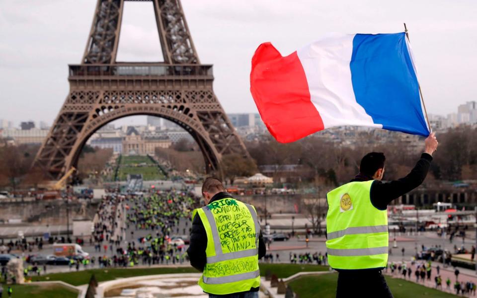 A Yellow Vest protester holds a French flag in front of the Eiffel Tower on February 9, 2019 in Paris - THOMAS SAMSON/AFP