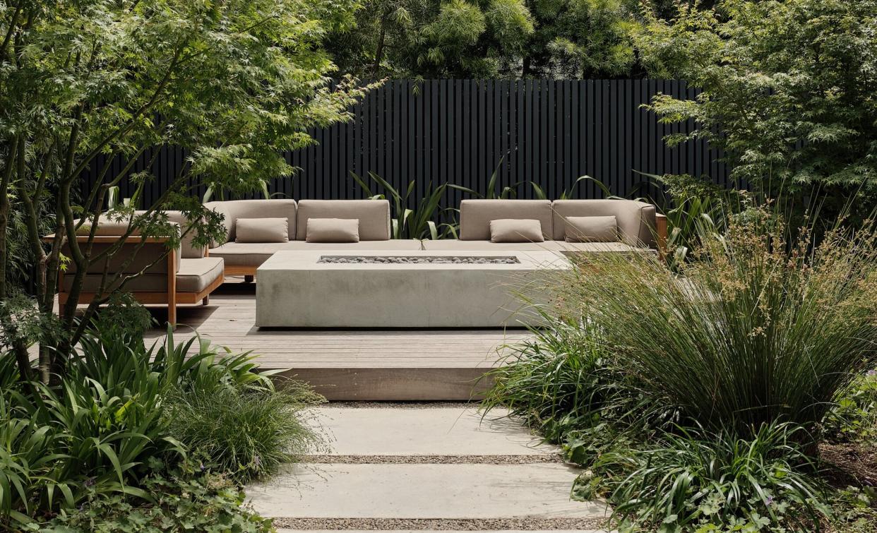  A backyard with concrete firepit and wooden furniture. 