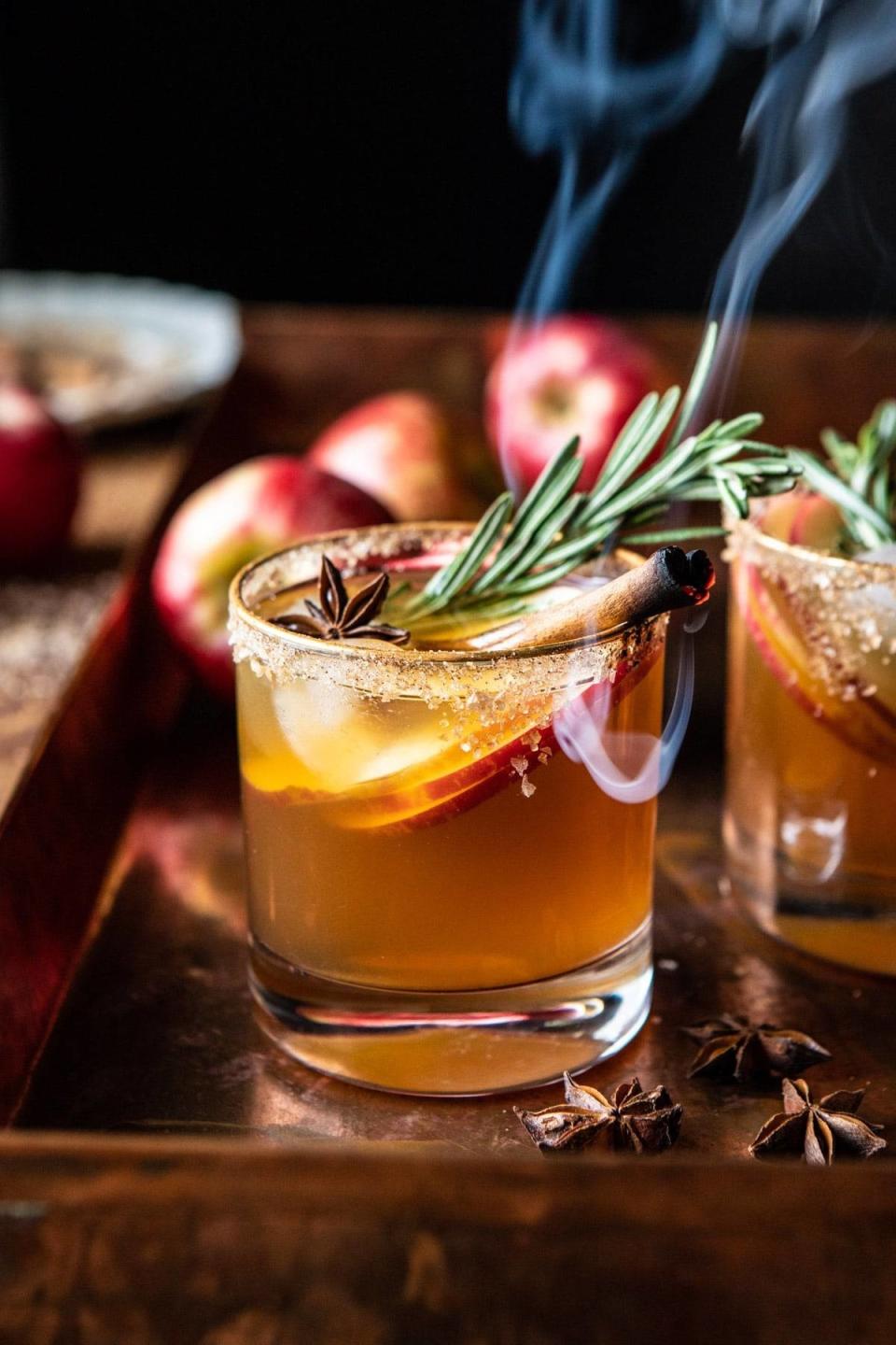 an apple cider margarita garnished with a smoked cinnamon stick and sprig of rosemary