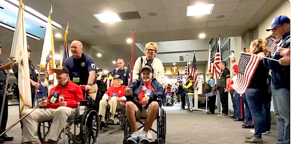 Veterans move past a Fire Department honor guard and well-wishers at Rhode Island International T.F. Green Airport on an early morning in June, en route to their flight to Washington, D.C.