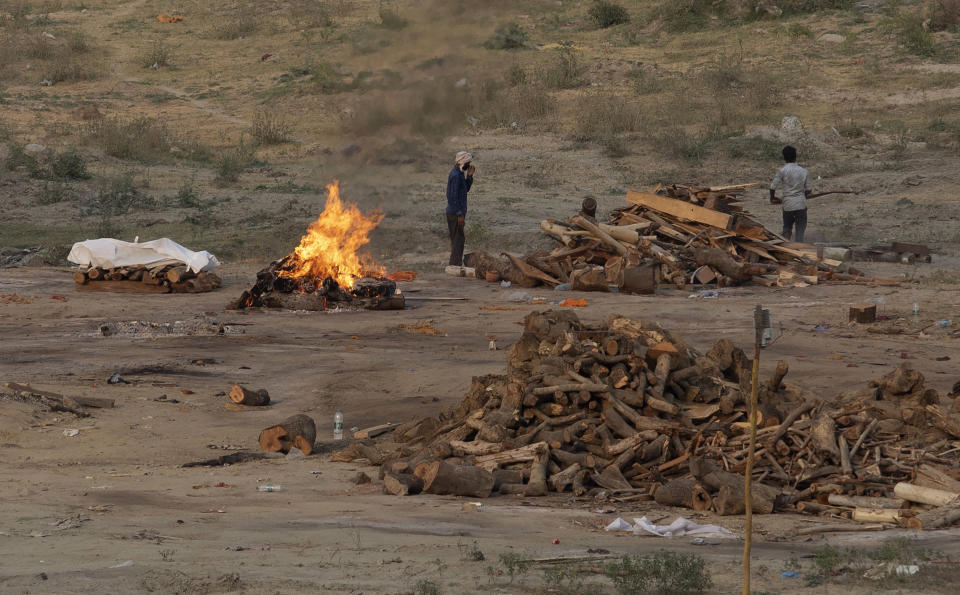 Body of a COVID-19 victim lies covered in white cloth next to a burning pyre of another victim at a cremation ground in Prayagraj, India, Saturday, May 1, 2021. India on Saturday set yet another daily global record with 401,993 new cases, taking its tally to more than 19.1 million. Another 3,523 people died in the past 24 hours, raising the overall fatalities to 211,853, according to the Health Ministry. Experts believe both figures are an undercount. (AP Photo/Rajesh Kumar Singh)